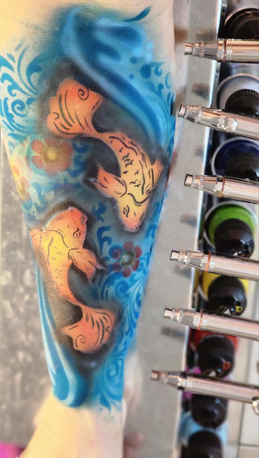 Airbrushed koi fish design in blue and orange beside a rack of airbrush guns