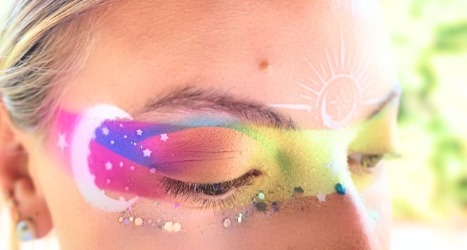 Rainbow festival eye makeup with glitter, gems and a white sun motif at the temple