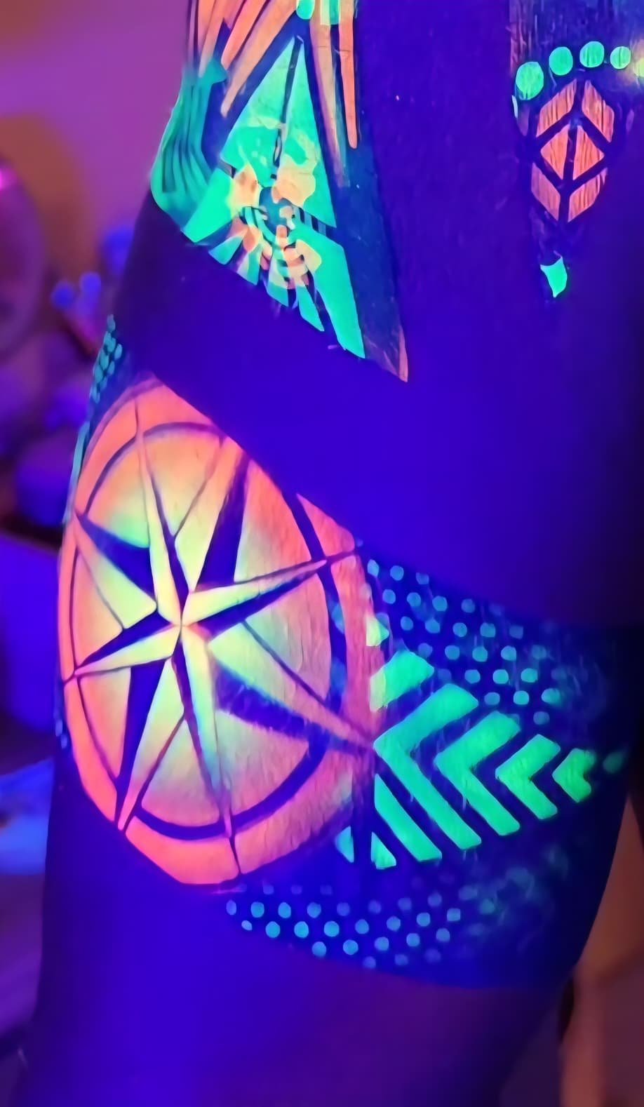UV body paint glowing under blacklight, a neon compass star with chevron detailing